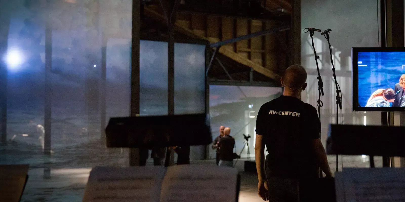 AV technician setting up equipment at a live event with screens and microphones