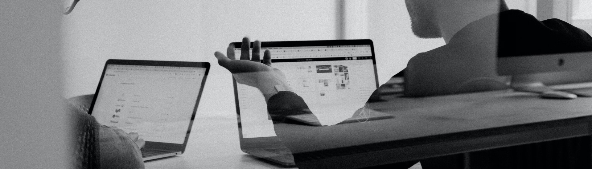 People working at laptops around a desk in an office, in black and white